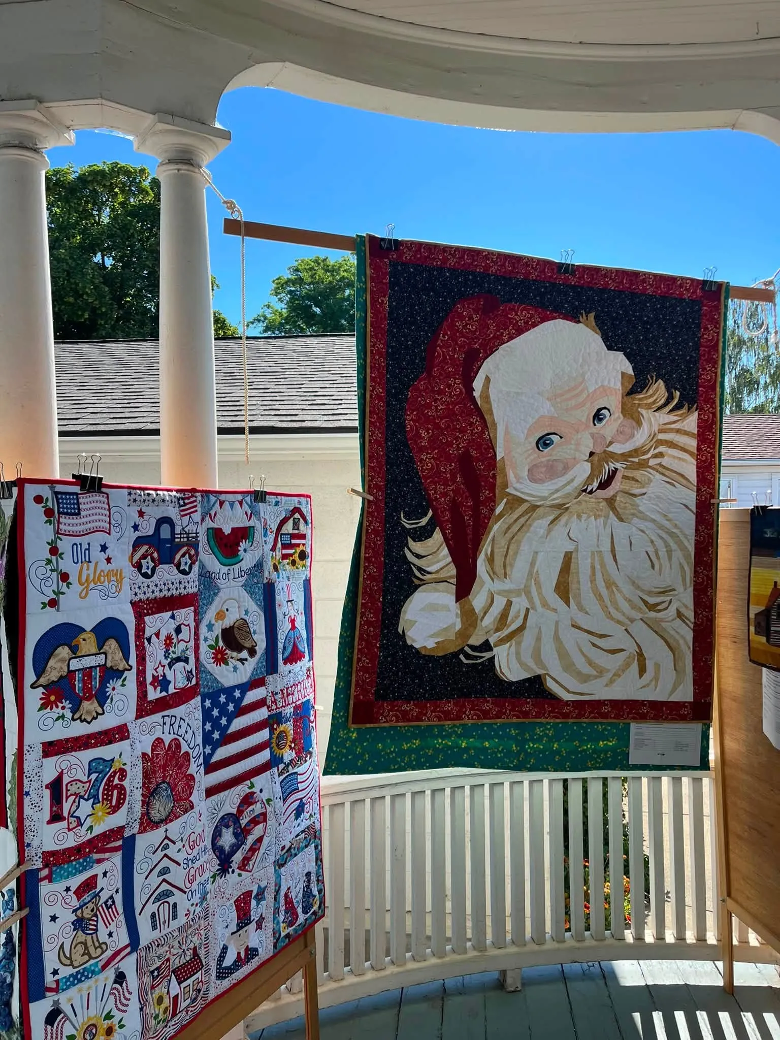 Santa Claus quilt and a patriotic sampler quilt hanging on the museum porch